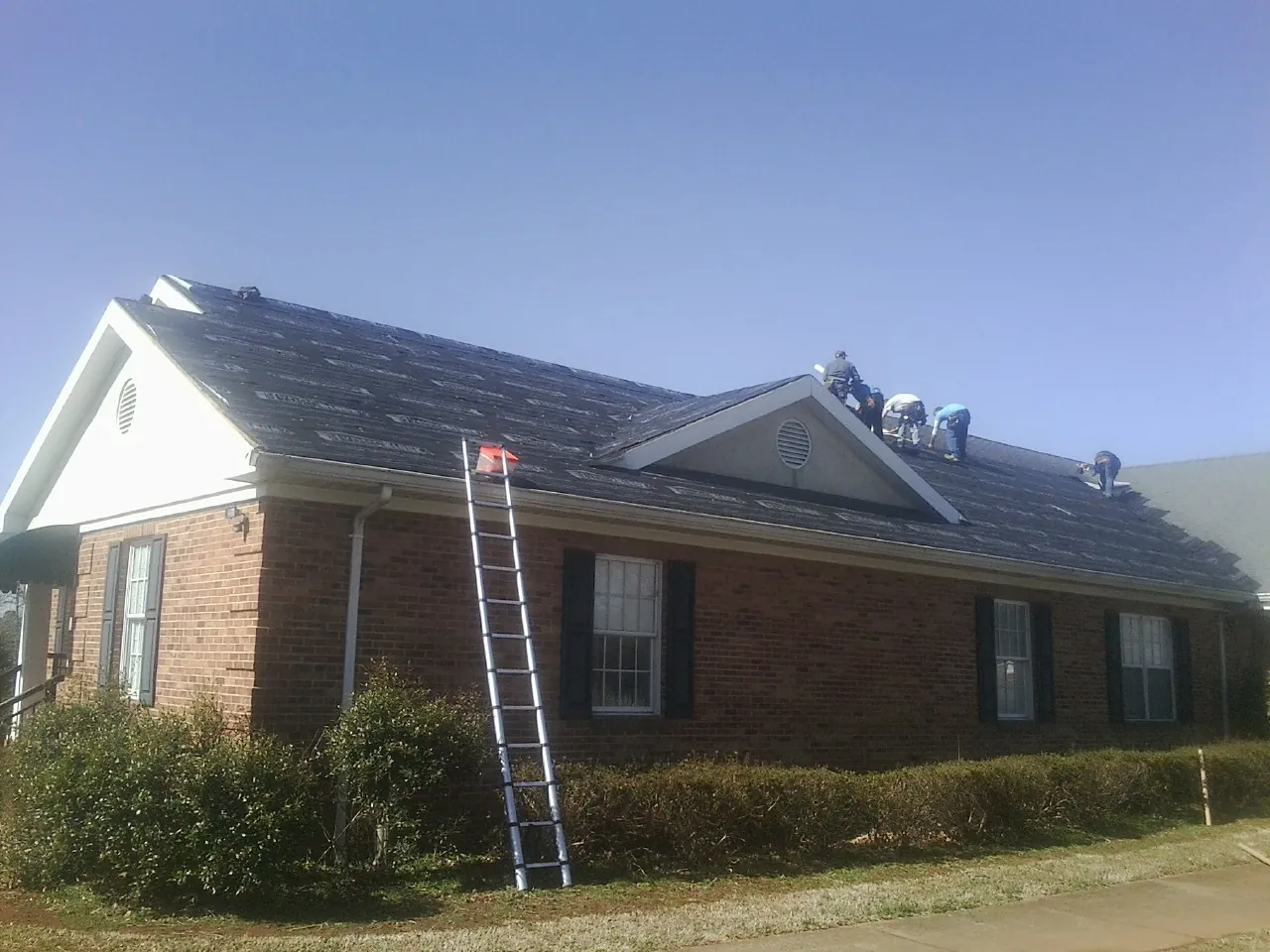 Crew tearing shingles off a brick ranch roof with a ladder set — Emergency Roof Repair work by our crew in Donnelly