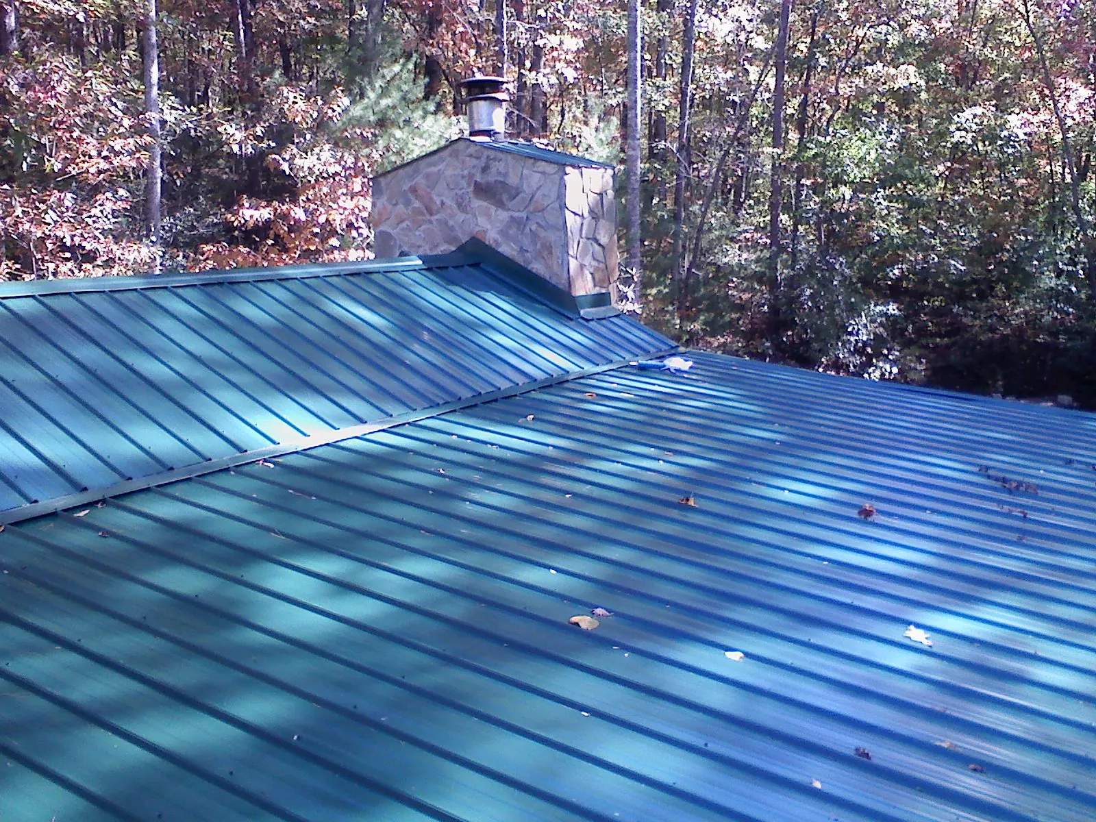 New green metal roof and stone chimney surrounded by autumn woods in Donnelly